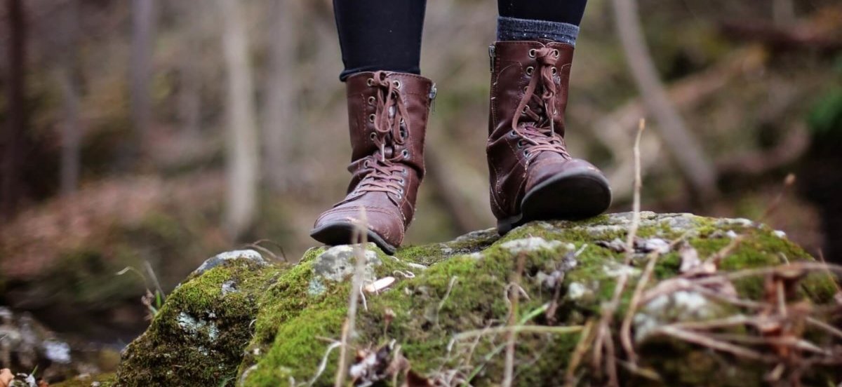 Female hiker standing on a large rock in the woods. Photo by Leah Kelley.