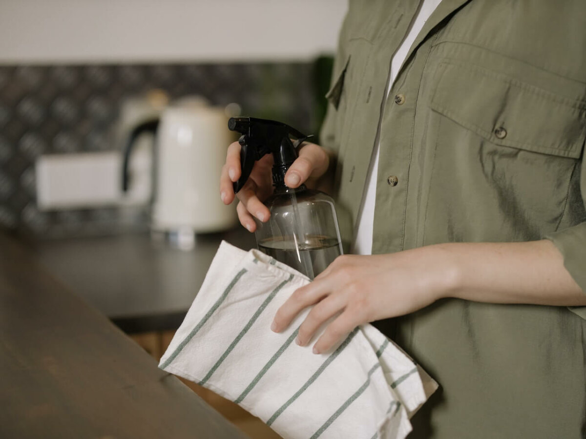 Woman in kitchen holding a spray cleaner and towel. Image credit: cottonbro