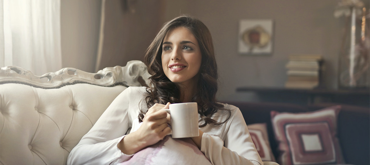 Woman sitting on a couch drinking coffee. Image credit: Andrea Piacquadio