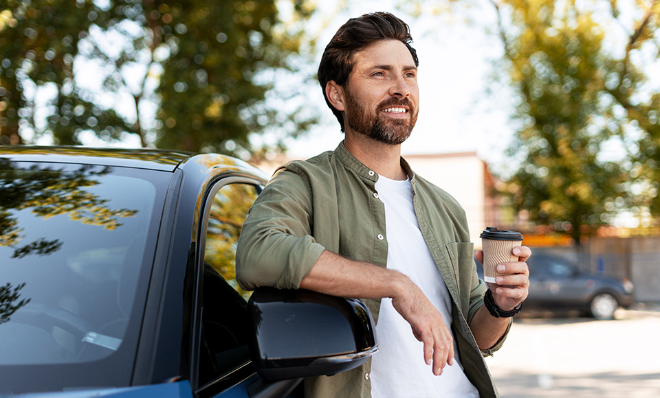 A man leaning on a car drinking coffee